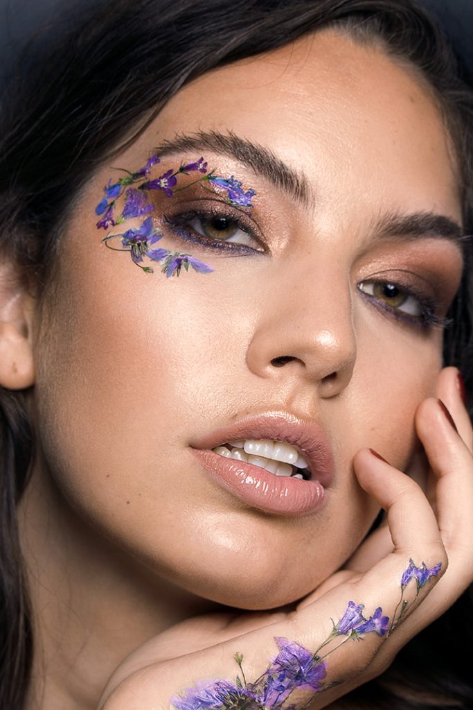 Model is Dimitra Lyras, wearing blue and purple flowers on her face and hand.