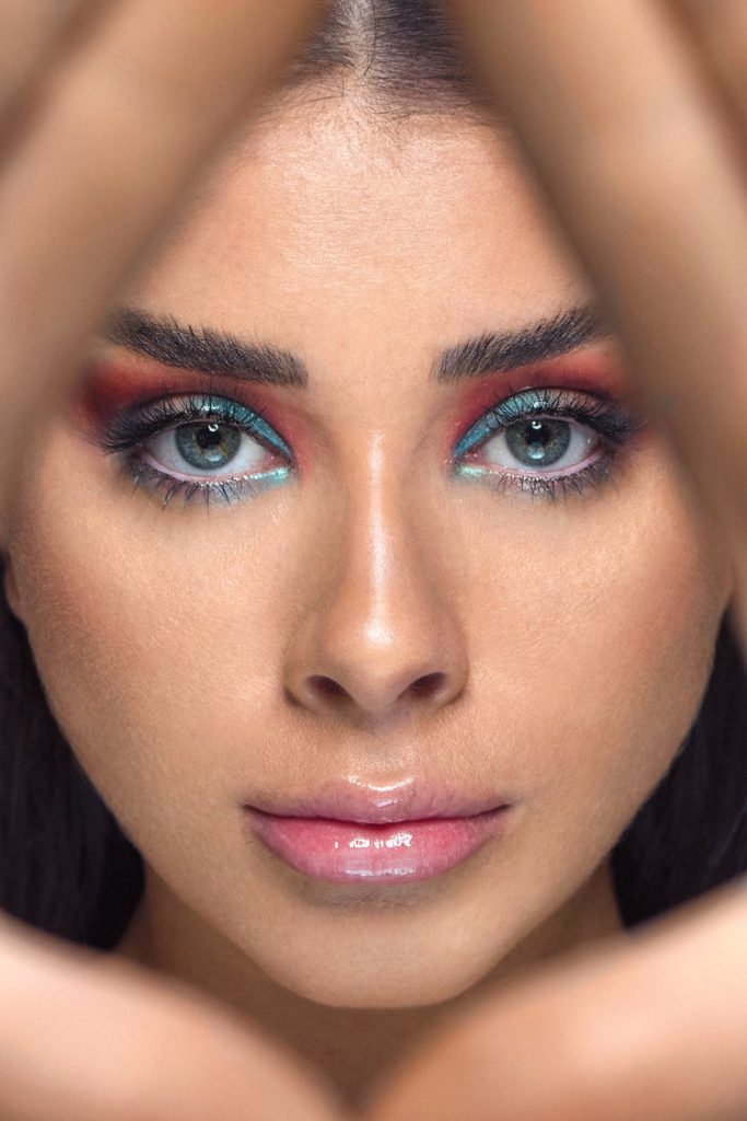 Model Alivia Celio with blue and red eyeshadow looking through her hands.