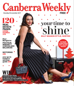 A brunette model wearing a pleated black satin dress, sitting on large presents.