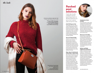 A redheaded model wearing a red knit jumper, tucked into black jeans with a brown handbag.