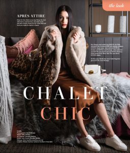 A brunette model sitting on a fake fur on a lounge chair wearing a brown satin dress and fake fur jacket.