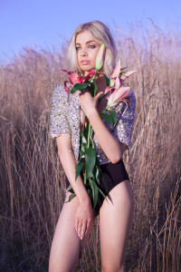 A blonde model holding a bunch of flowers, wearing black underwear in front of long grass.