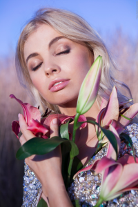 A blonde model with her eyes closed holding a bunch of flowers.
