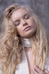 A blonde model with her eyes closed and a piece of netting over her face.