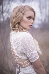A blonde model with her hair in a braid wearing a white dress that laces up at the back.