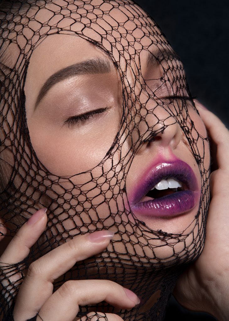 Model Jordan De Alvia with purple smeared lipstick and a black fishnet stocking over her face.